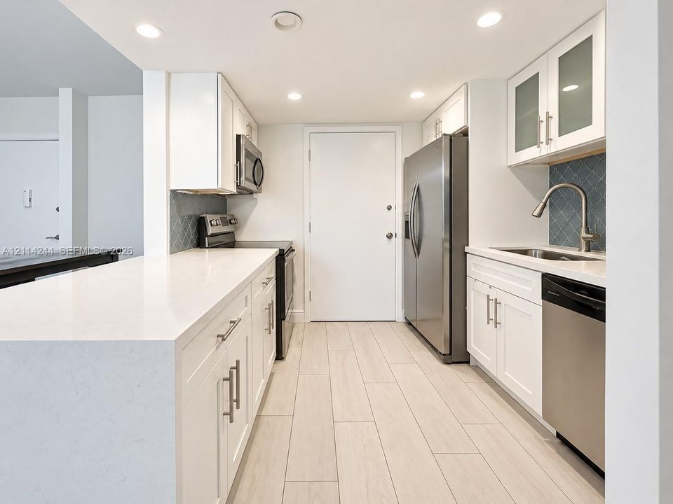 Kitchen featuring white shaker-style cabinetry, quartz countertops, blue geometric tile backsplash, stainless steel appliances.
