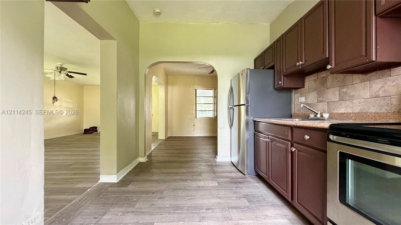 Kitchen featuring dark wood-finish cabinetry, stainless steel appliances, neutral tile backsplash, and wood-finish flooring with arched architectural detailing