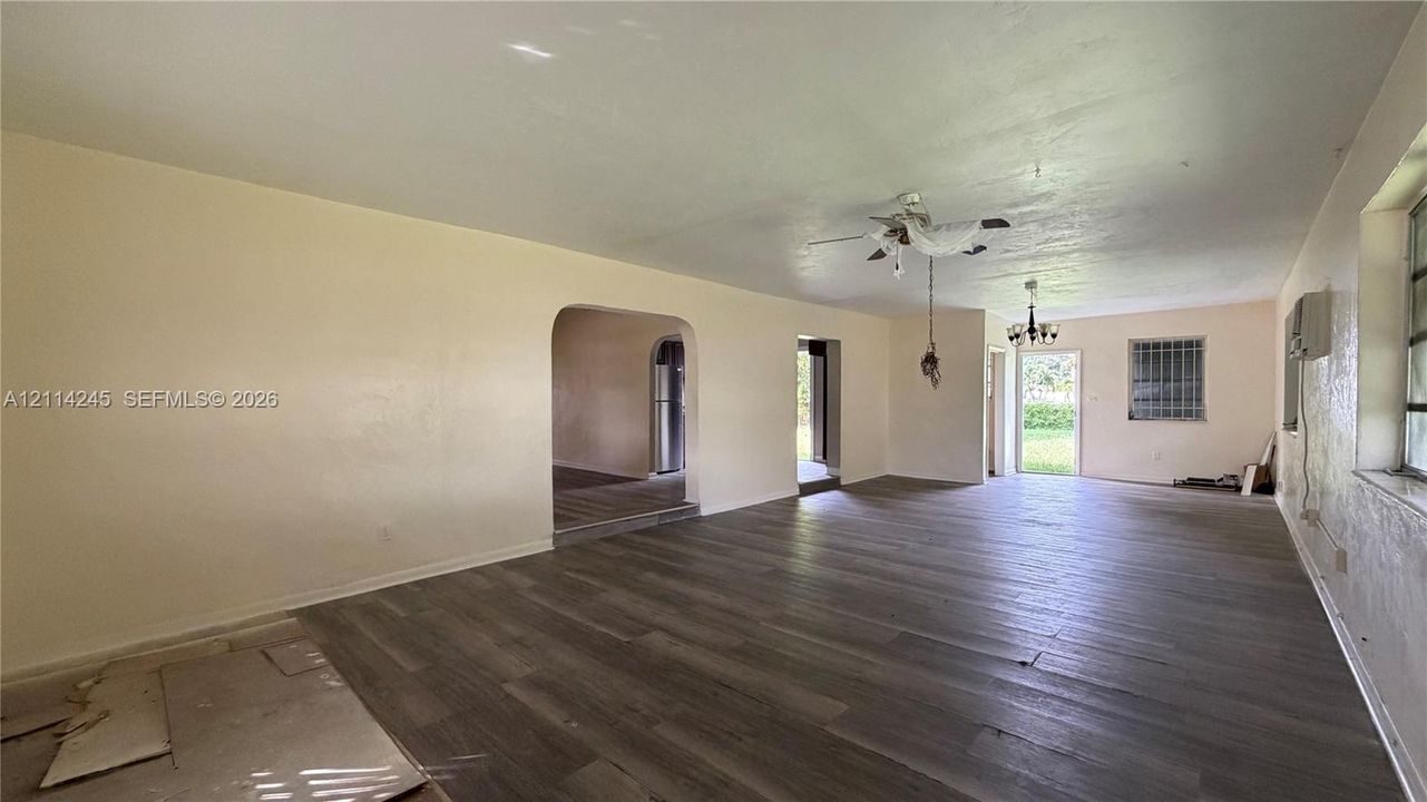 Spacious interior featuring wood-finish flooring, an arched doorway, a ceiling fan with integrated lighting, and a multi-light chandelier