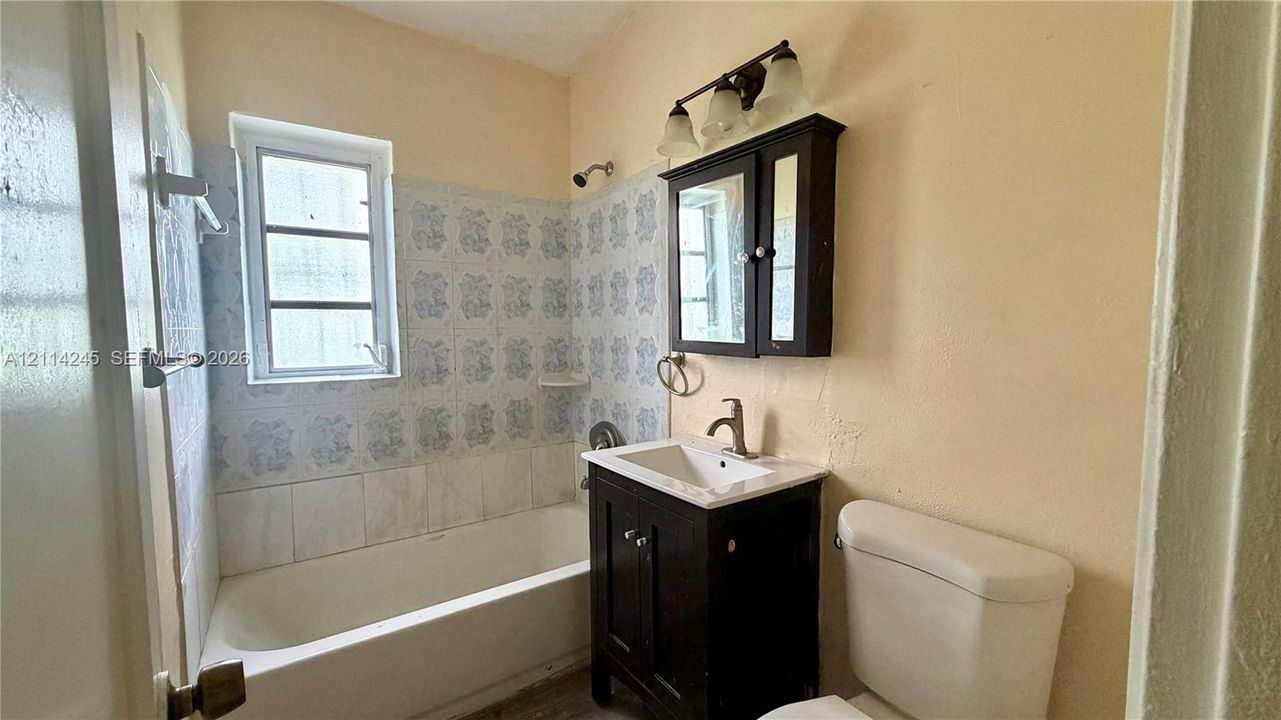Bathroom featuring a tub-shower combination with patterned wall tile, vanity cabinet with a integrated sink, three-light wall-mounted fixture, and a surface-mounted medicine cabinet