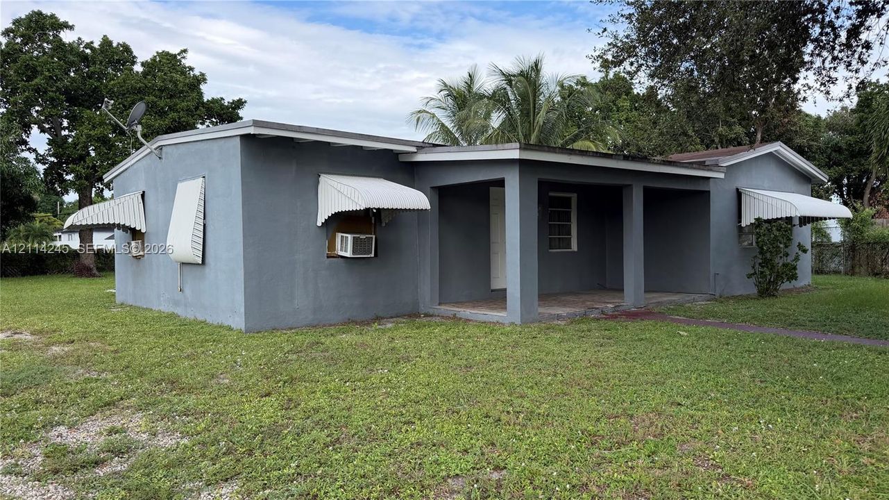 Stucco exterior featuring a covered front porch, low-slope roofline, and metal window awnings situated on a lot with mature trees