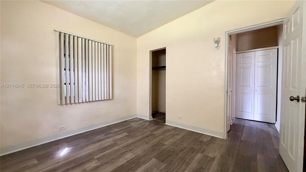 Room featuring wood-finish flooring, vertical window blinds, and dual-closet storage with white paneled doors