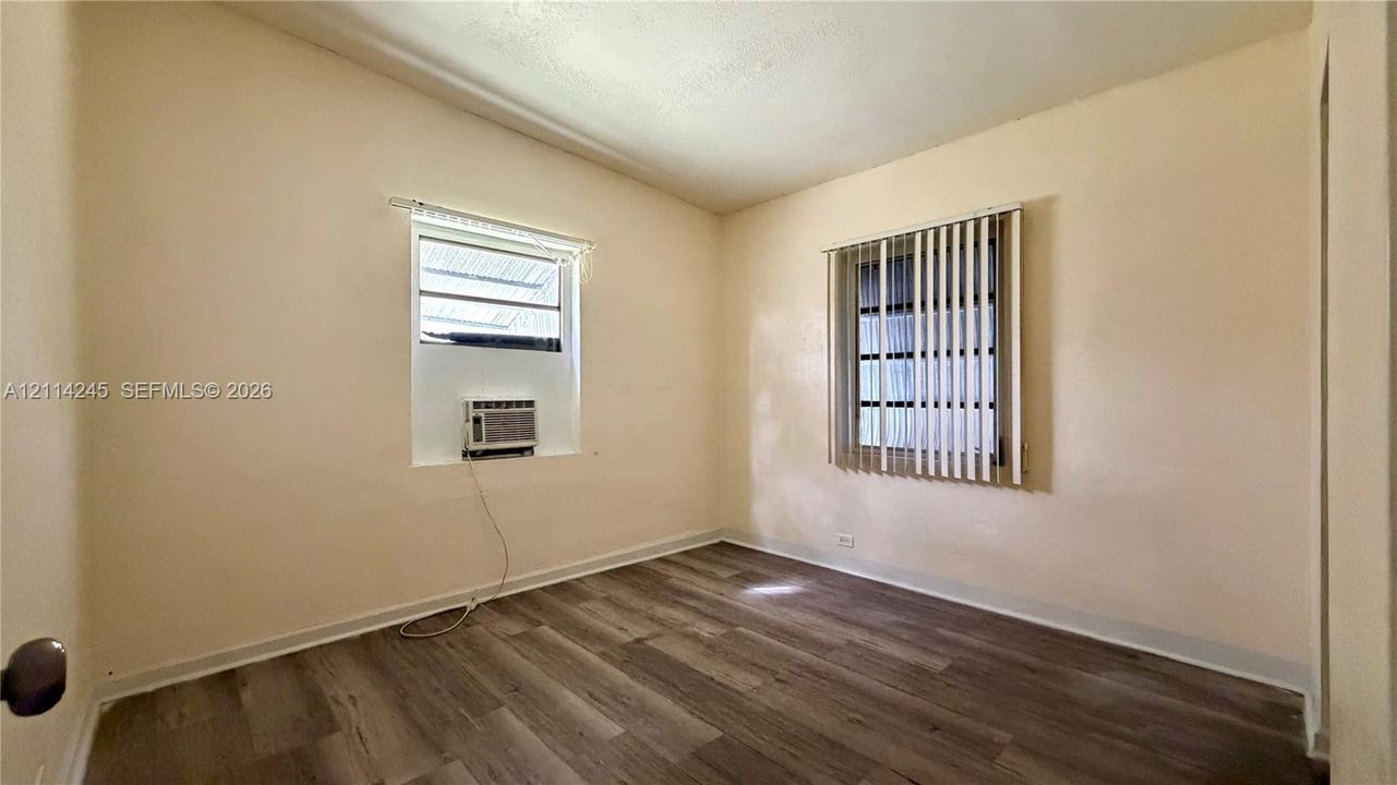 Room featuring wood-finish flooring, dual windows with vertical blinds, and a built-in wall-mounted air conditioning unit