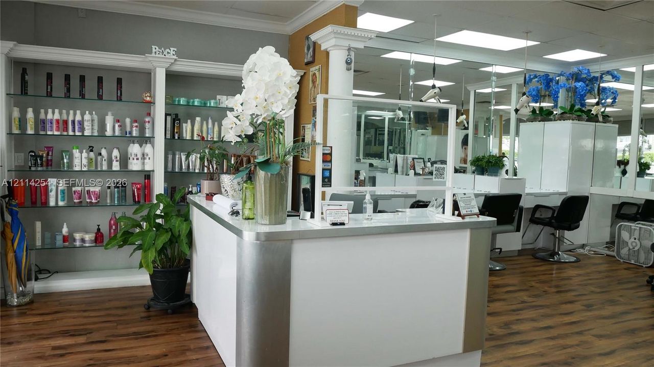 Reception area featuring a white laminate desk with metallic trim, built-in glass shelving, wood-finish flooring, and a structural column