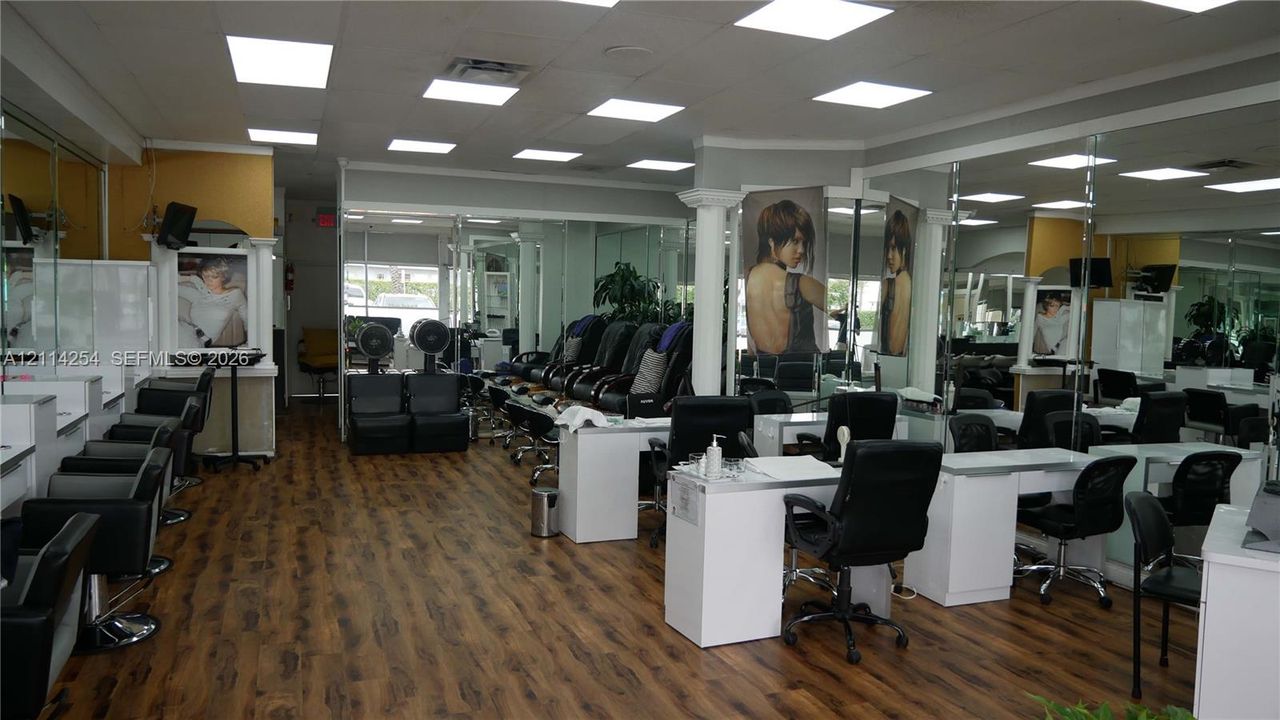 Spacious interior featuring wood-finish flooring, recessed LED panel lighting, extensive wall-to-wall mirrors, and multiple built-in workstations