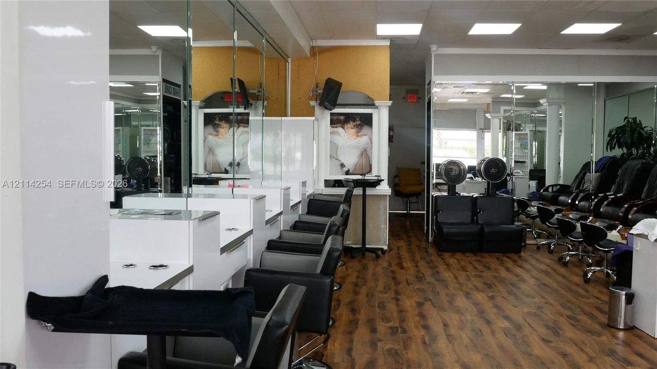 Commercial interior featuring wood-finish flooring, extensive wall-to-wall mirrors, recessed lighting, and built-in white cabinetry workstations