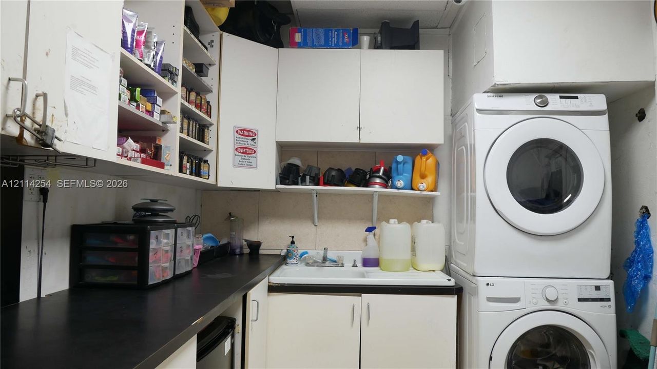 Laundry area featuring white cabinetry, a built-in utility sink, solid-surface countertop, and stacked washer and dryer