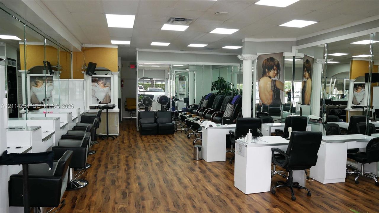Commercial space featuring wood-finish flooring, extensive wall-to-wall mirrors, recessed LED lighting, and built-in service stations with white cabinetry