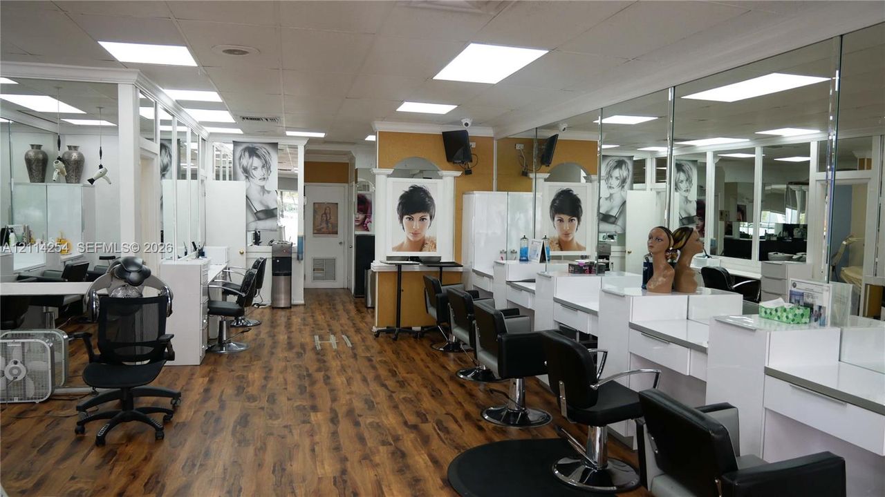 Commercial space featuring wood-finish flooring, extensive wall-to-wall mirrors, recessed lighting, and built-in white cabinetry workstations