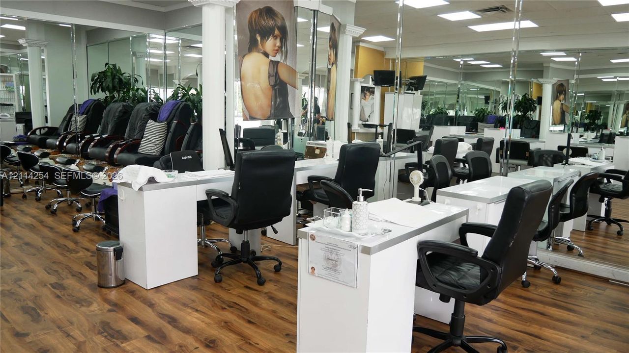 Commercial space featuring wood-finish flooring, extensive wall-to-wall mirrors, recessed lighting, and built-in service stations