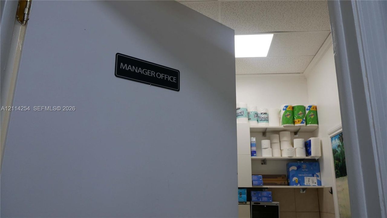 Solid-core door featuring a black plaque, drop ceiling with recessed lighting, and wall-mounted storage shelving