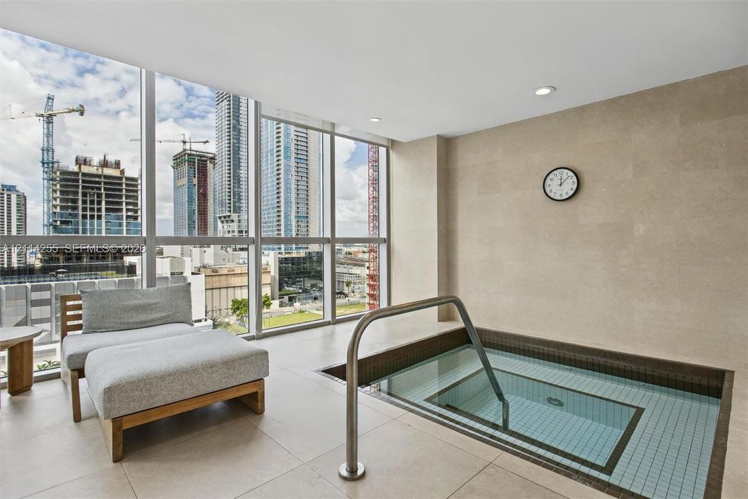 In-ground plunge pool with tile lining, stainless steel handrail, floor-to-ceiling windows, and large-format tile flooring