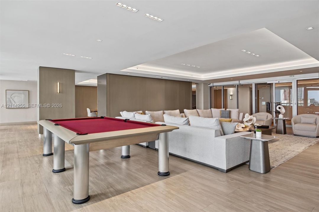 Open-concept interior featuring recessed ceiling lighting, tray ceiling detail with perimeter cove lighting, wood-finish flooring, and floor-to-ceiling glass panel doors