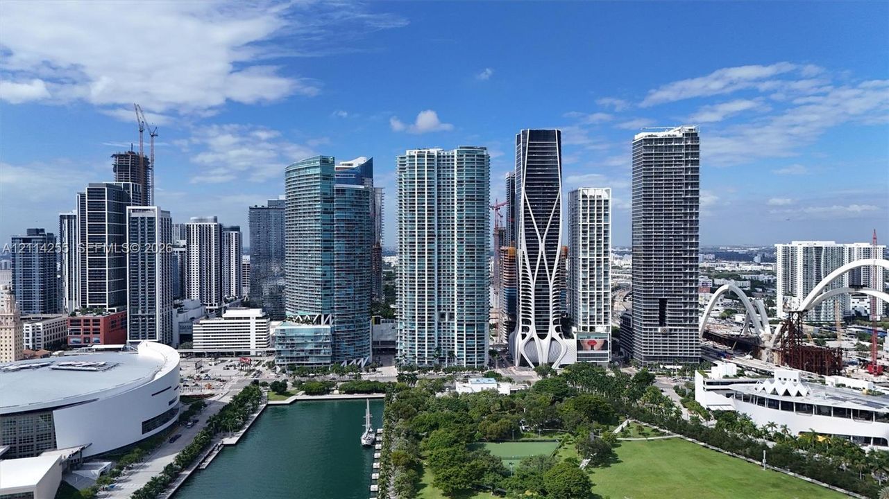 Aerial perspective of an urban center featuring high-rise glass-facade towers, manicured green space, and a waterfront basin