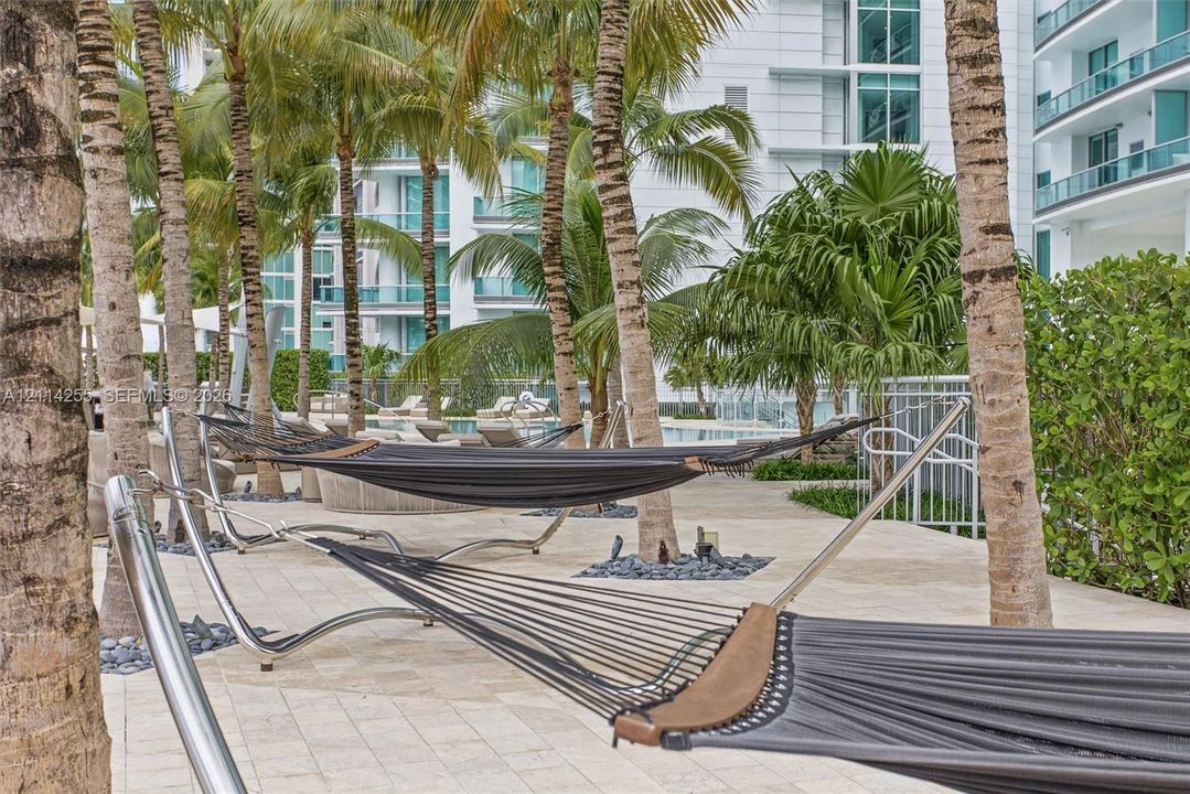 Outdoor terrace featuring light-colored stone paving, mature palm trees, and metal-framed hammock stands