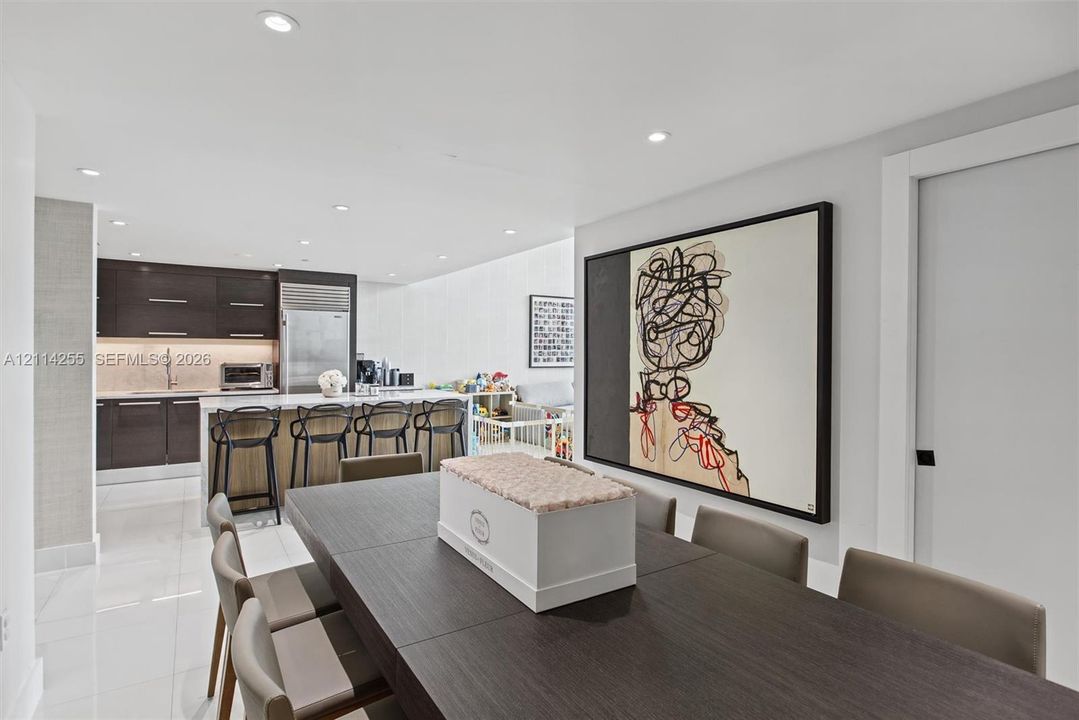 Open-concept kitchen featuring high-gloss dark cabinetry, integrated refrigerator, stone countertops, and recessed lighting throughout