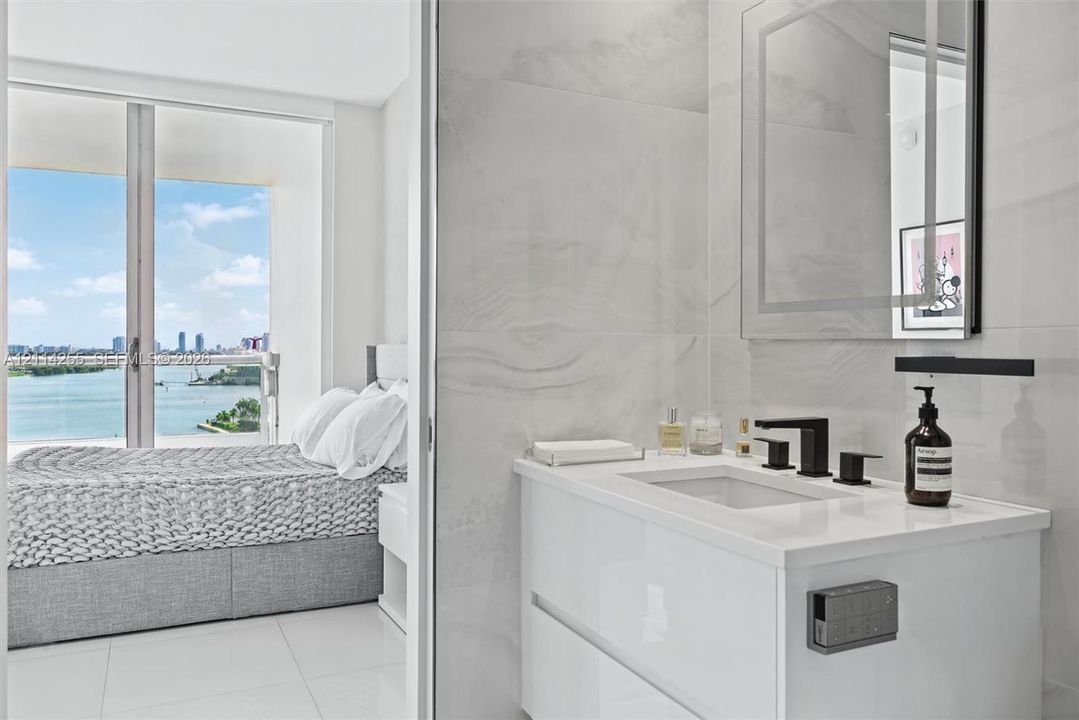 Modern floating vanity with a solid-surface countertop, rectangular basin, and matte black faucet, featuring wall-to-wall large-format porcelain tile, a backlit mirror, and floor-to-ceiling glass sliding doors