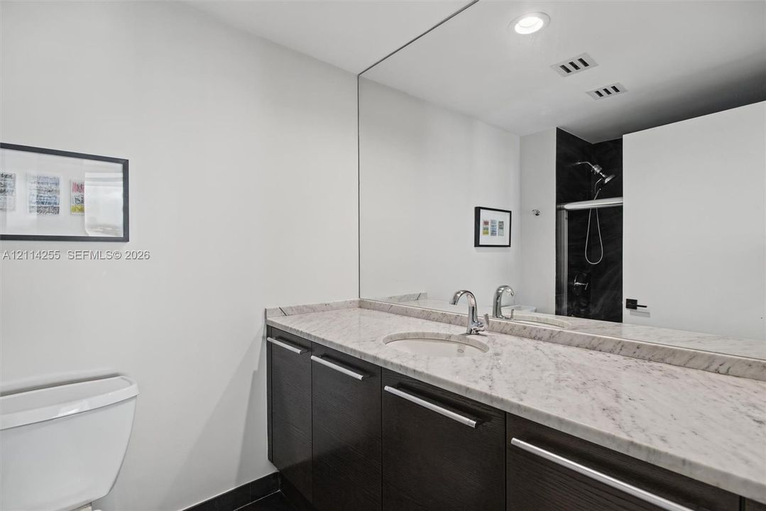 Bathroom featuring dark wood-finish cabinetry, stone countertop with an integrated oval sink, chrome faucet, expansive wall-to-wall mirror, and recessed lighting