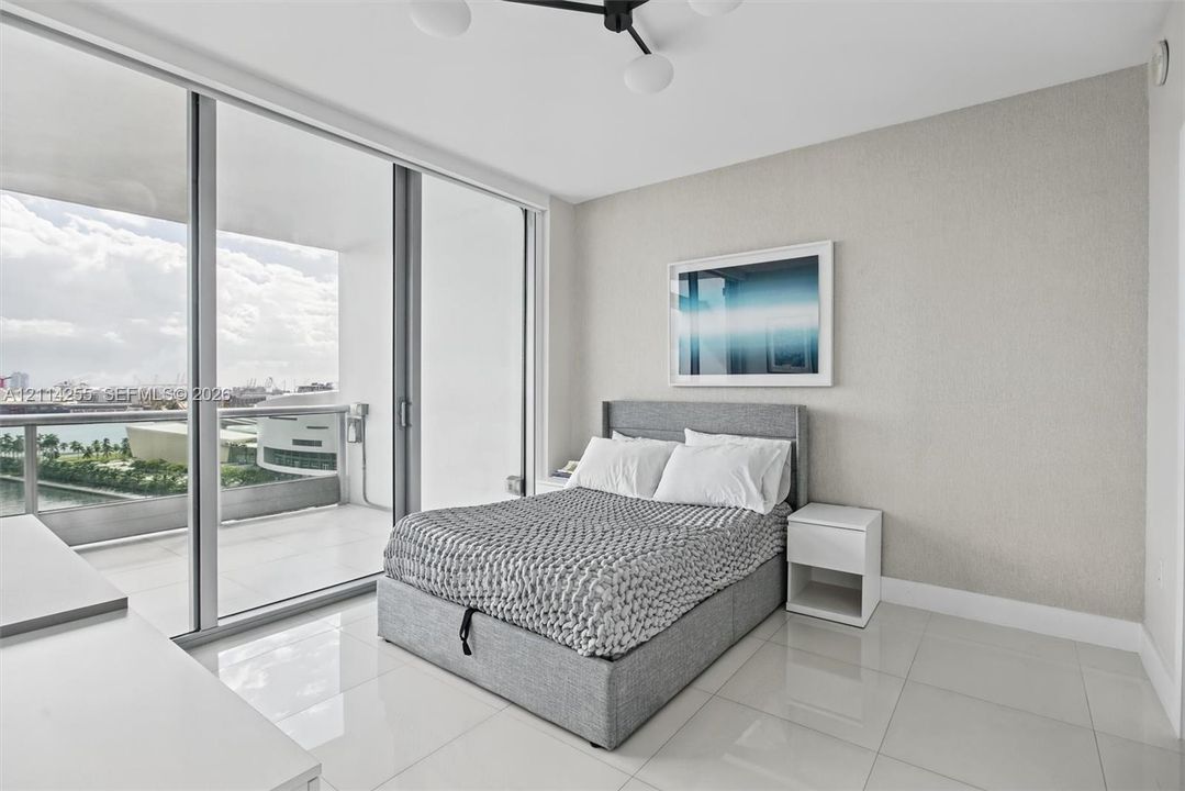 Floor-to-ceiling glass sliding doors, private balcony, neutral wall finish, light-colored tile flooring, and contemporary multi-arm overhead light fixture