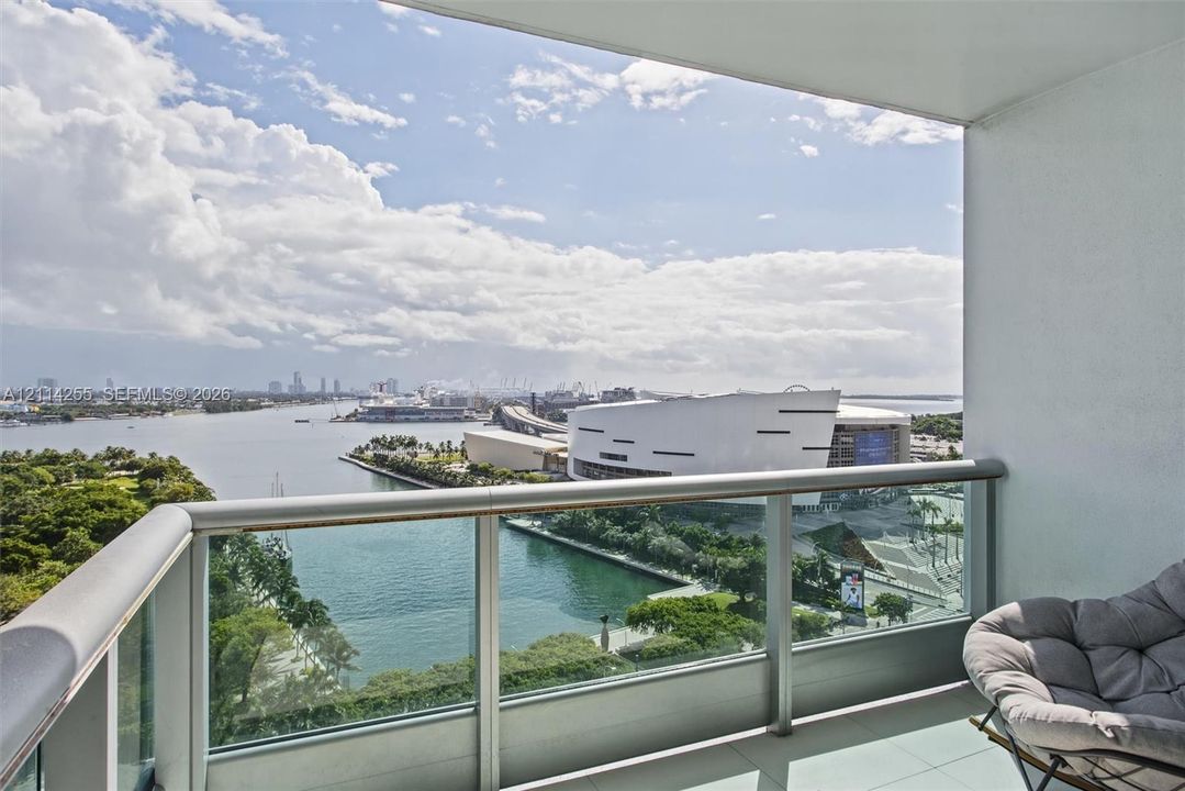 Covered balcony featuring a glass panel railing, metal frame, and tile flooring, oriented toward a water and city skyline horizon