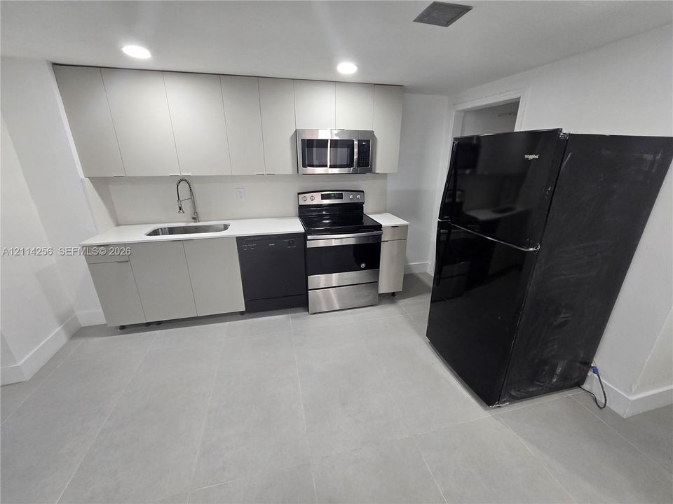 Kitchen featuring light-toned cabinetry, solid-surface countertops, recessed lighting, large-format tile flooring, and integrated stainless steel appliances