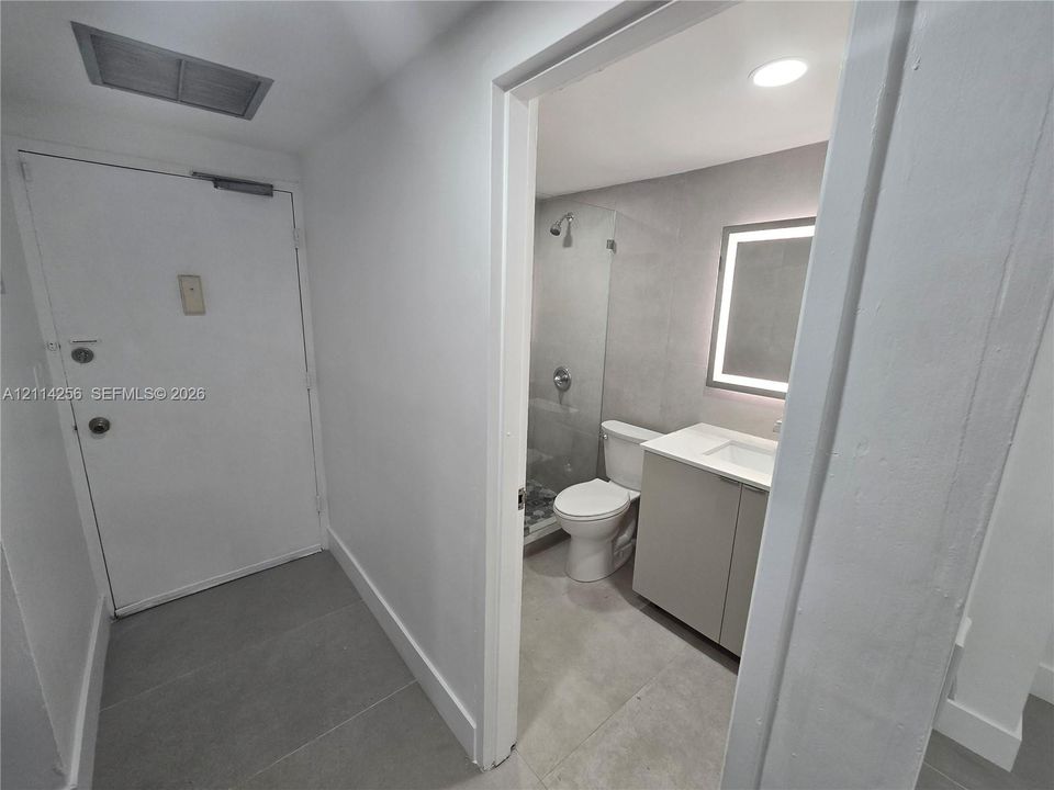 Bathroom featuring a glass-enclosed shower, vanity with integrated basin, stone-finish countertop, and LED-backlit mirror