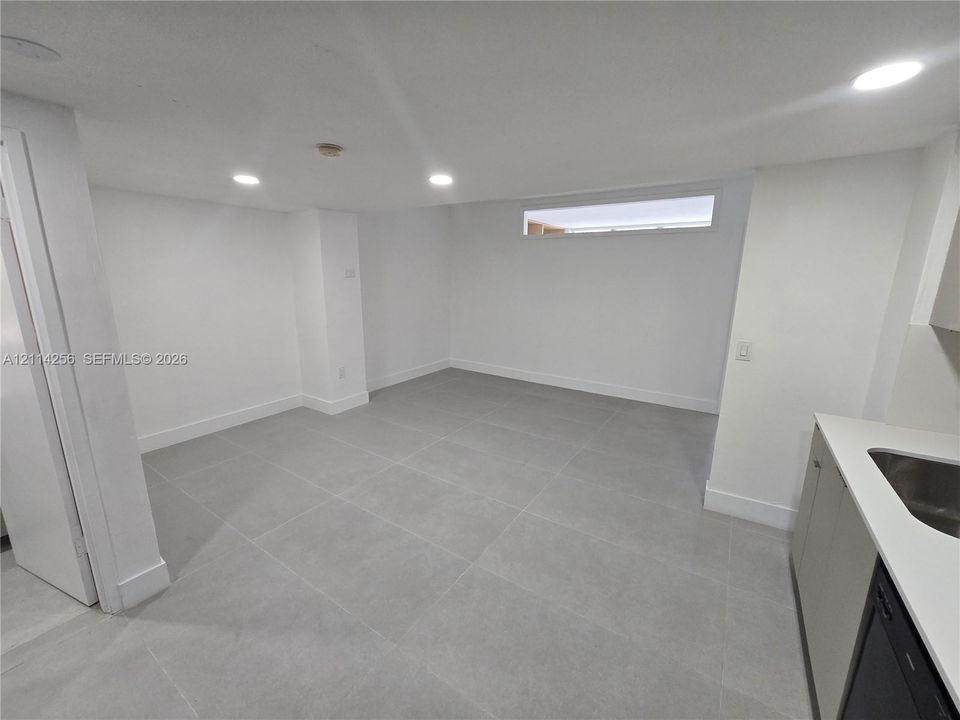 Interior space featuring large-format ceramic tile flooring, recessed LED lighting, a rectangular horizontal transom window, and a built-in cabinetry unit with a solid-surface countertop and integrated stainless steel sink