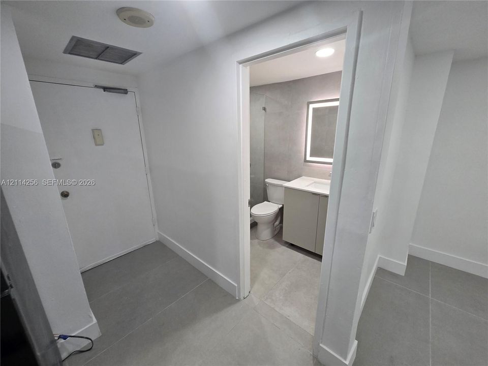 Bathroom featuring light-toned cabinetry, a modern vanity with integrated sink, a frameless glass shower enclosure, a LED-backlit vanity mirror, and large-format neutral-toned floor tile
