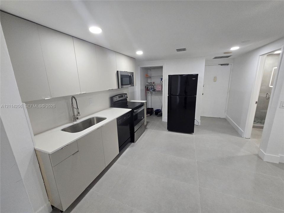 Kitchen featuring flat-panel cabinetry, quartz countertops, an undermount stainless steel sink with a high-arc faucet, integrated black appliances, and large-format tile flooring
