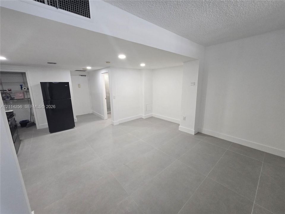 Neutral-toned large-format tile flooring, recessed ceiling lighting, and a full-size black refrigerator