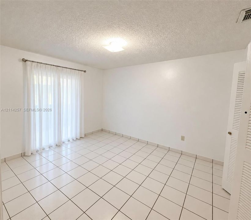 Interior space featuring ceramic tile flooring, a flush-mount ceiling light, sliding glass doors, and a louvered closet door