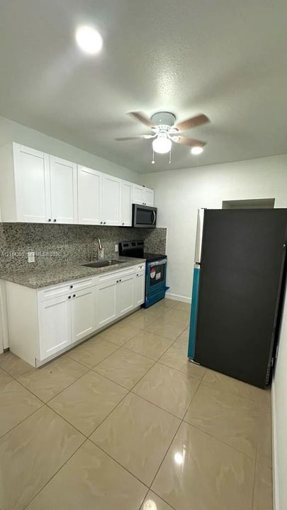 Kitchen featuring white cabinetry, stone-finish countertops, tile flooring, and built-in appliances including a microwave, range, and refrigerator