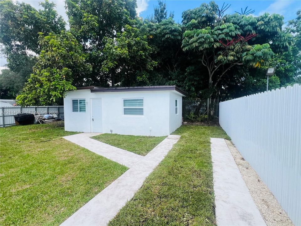 Detached structure featuring a white exterior, horizontal sliding windows, a concrete walkway, and white perimeter fencing