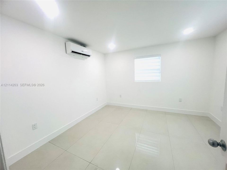 Interior space featuring large-format tile flooring, recessed ceiling lighting, a wall-mounted ductless air conditioning unit, and a window with horizontal blinds