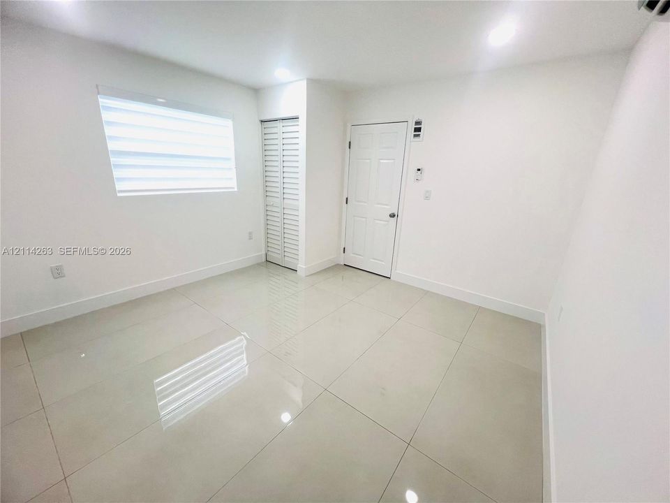 Interior room featuring large-format polished tile flooring, recessed ceiling lighting, a louvered-door closet, and a multi-panel interior door