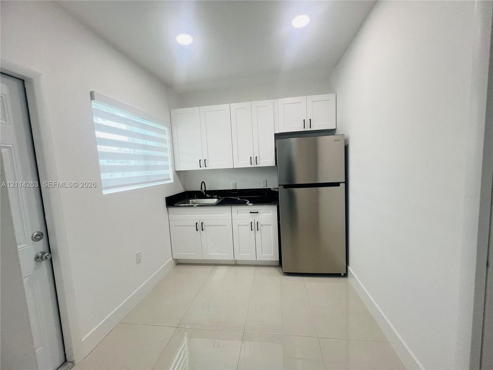 Kitchenette featuring white shaker-style cabinetry, high-contrast dark stone countertops, stainless steel refrigerator, undermount sink with matte black hardware, and tile flooring