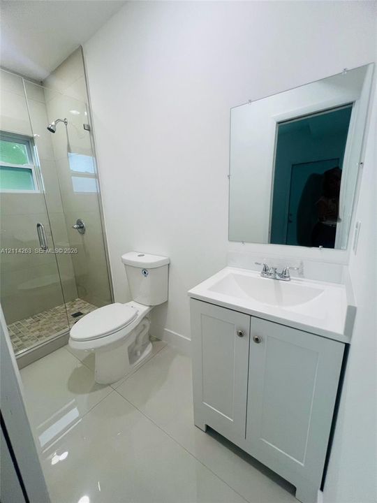 Bathroom featuring a white vanity cabinet with a integrated sink, a frameless glass shower enclosure, large-format tile flooring, and a wall-mounted mirror