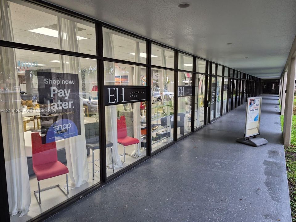 Expansive floor-to-ceiling glass storefront featuring dark-toned metal framing, recessed lighting, and a continuous covered concrete walkway