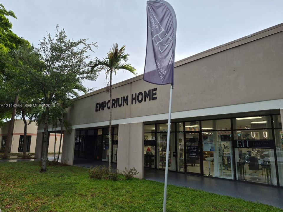 Commercial exterior featuring a concrete facade, expansive floor-to-ceiling glass storefront, and palm tree landscaping