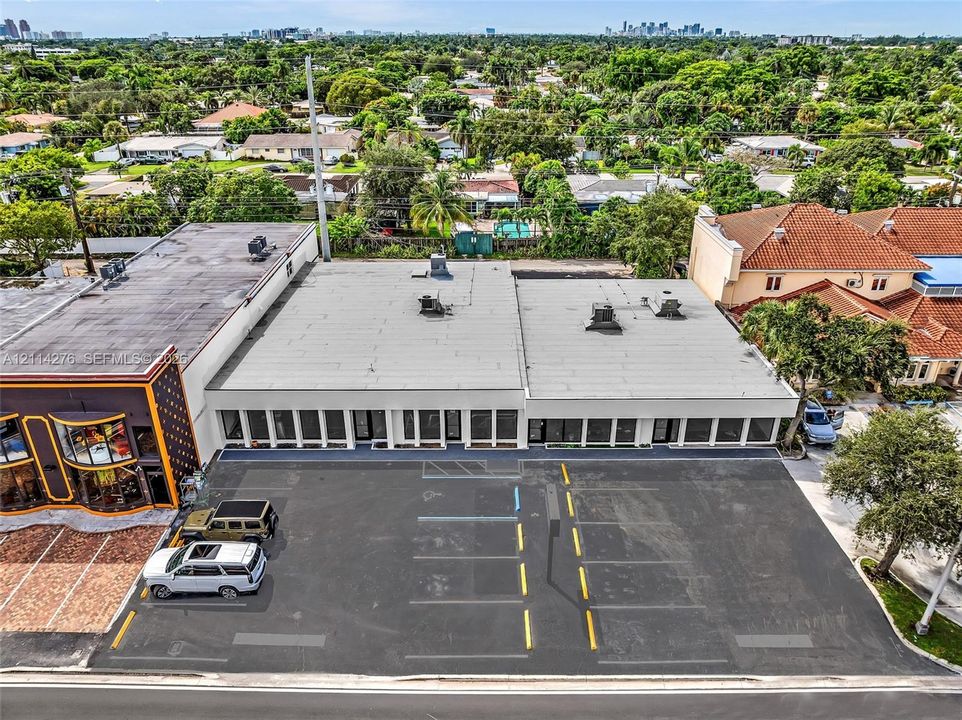 Commercial property exterior featuring a dedicated asphalt parking lot with marked stalls, multiple glass-paneled storefront entrances, and a flat roof system