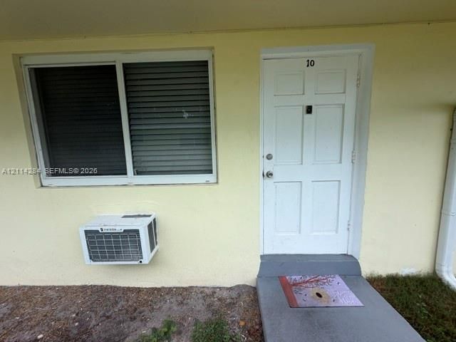 Exterior entry featuring a six-panel door, horizontal sliding window, and wall-mounted air conditioning unit