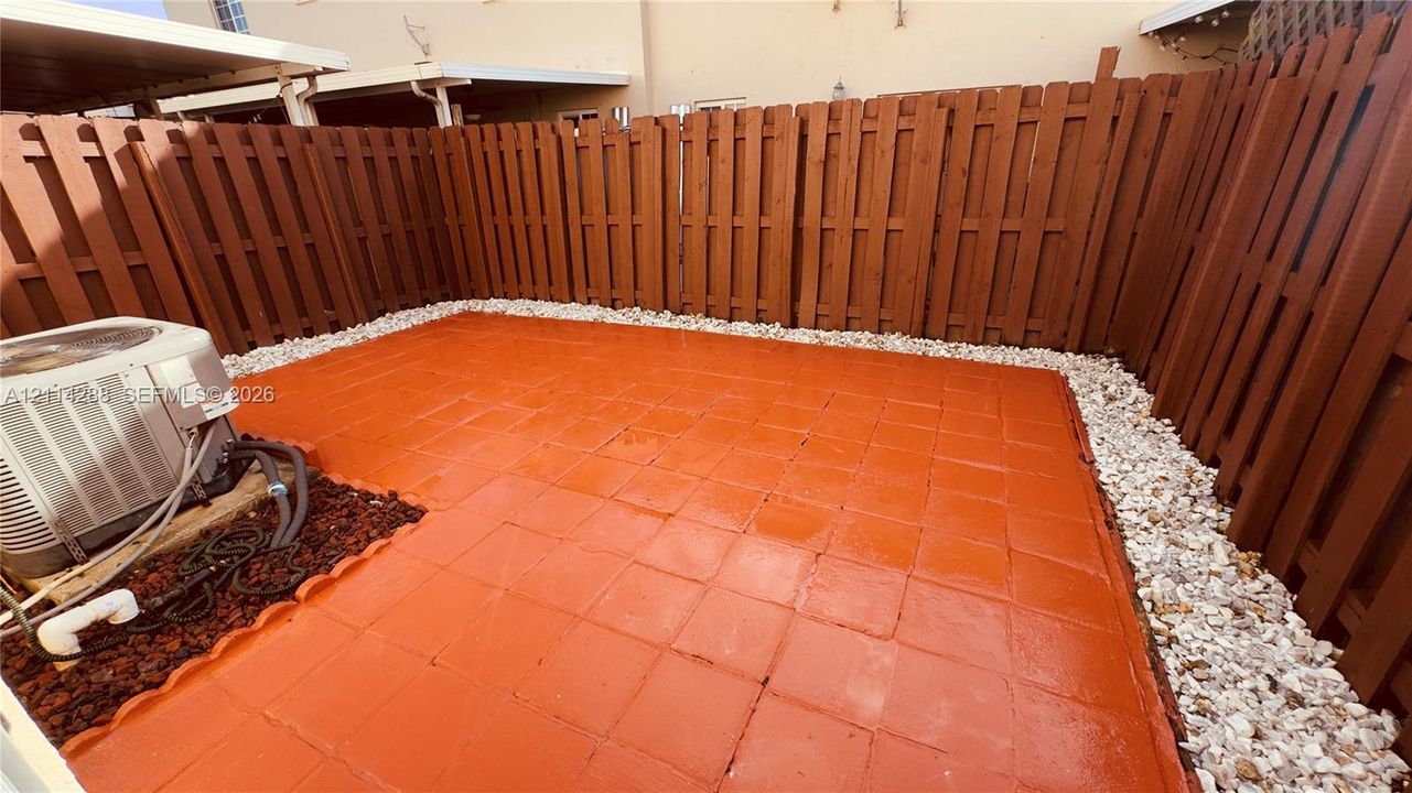 Enclosed patio featuring square paver flooring, a perimeter of light-colored decorative stone, and a wood-slat privacy fence