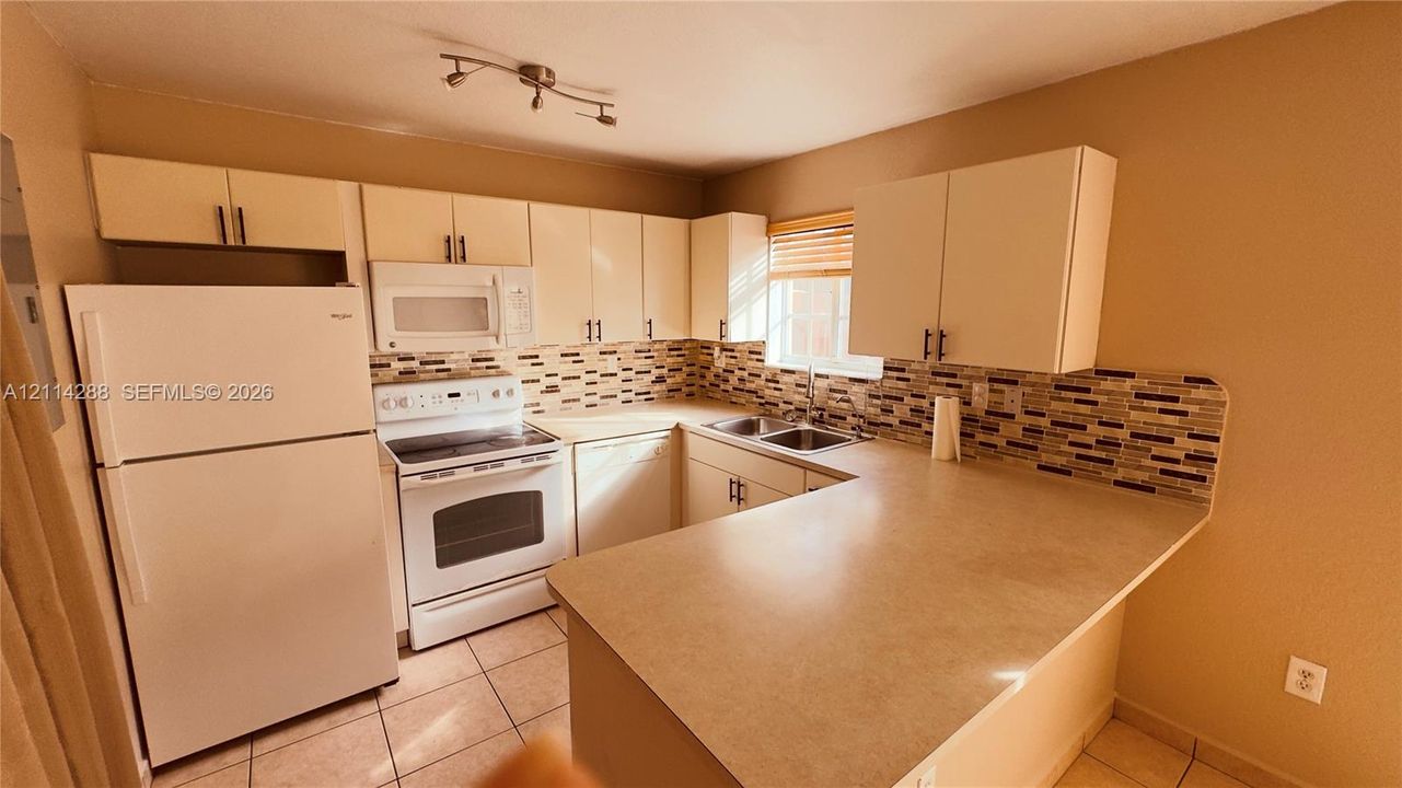 Kitchen featuring cabinetry with hardware, laminate countertops, mosaic tile backsplash, double-basin stainless steel sink, and track lighting
