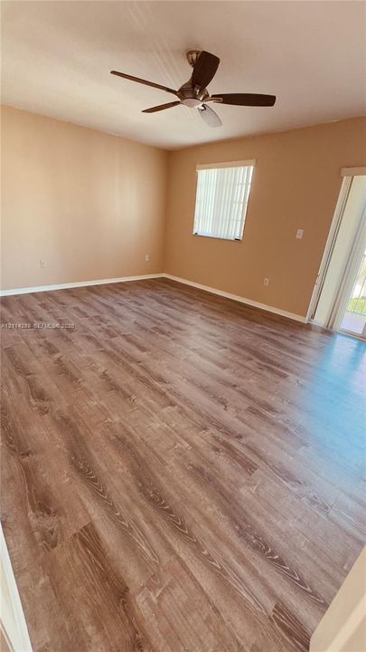 Wood-finish flooring, ceiling fan with integrated lighting, and window with vertical blinds