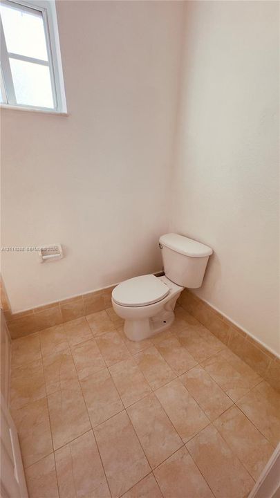 Restroom featuring a two-piece white porcelain toilet, ceramic tile flooring, matching ceramic tile wainscoting, and a multi-pane window