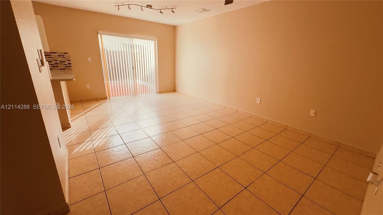 Neutral-toned interior space featuring ceramic tile flooring, a multi-head track lighting fixture, and a sliding glass door with vertical blinds