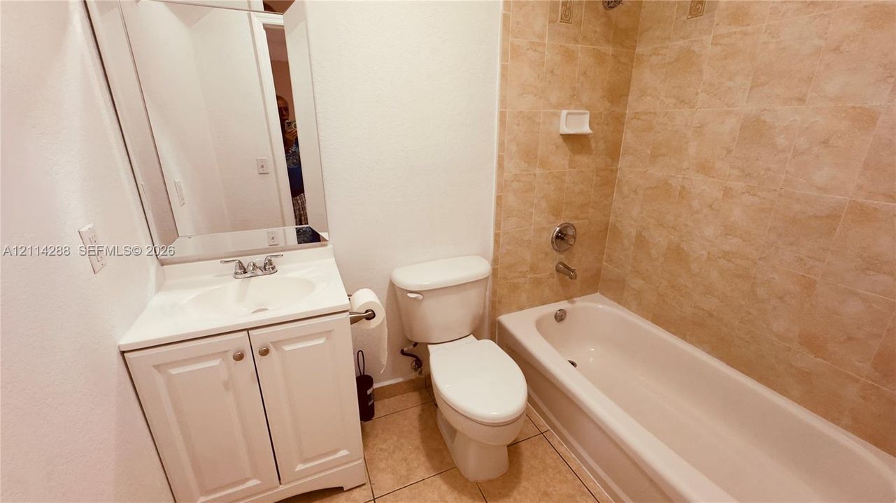 Bathroom featuring a white vanity cabinet with a integrated sink, a large wall-mounted mirror, ceramic tile flooring, and a bathtub enclosure with tile surround