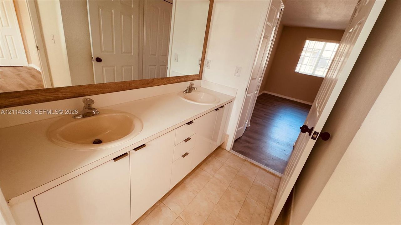 Dual-basin vanity featuring a solid-surface countertop, integrated sinks, white cabinetry, and a full-width mirror