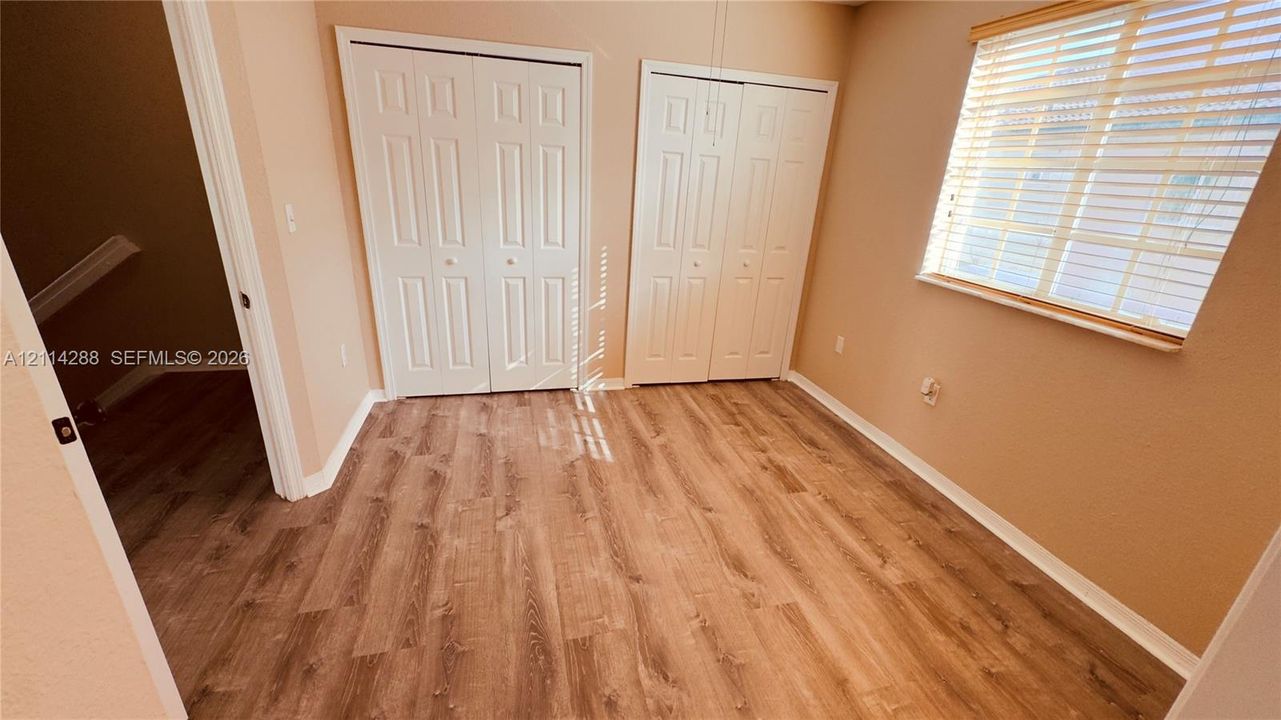 Wood-finish flooring, two dual-panel bi-fold closets, and a window with horizontal blinds