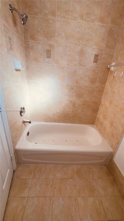 Bathtub surround featuring floor-to-ceiling neutral tile with decorative inlay accents, integrated jetted tub, wall-mounted showerhead, and matching floor tile